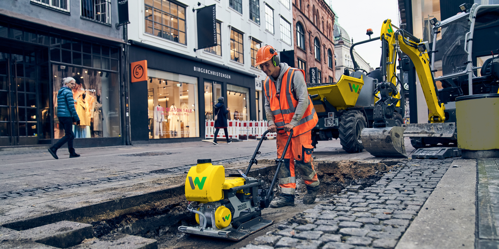 Un hombre trabajando en una obra en el centro de la ciudad con una plancha vibratoria ligera