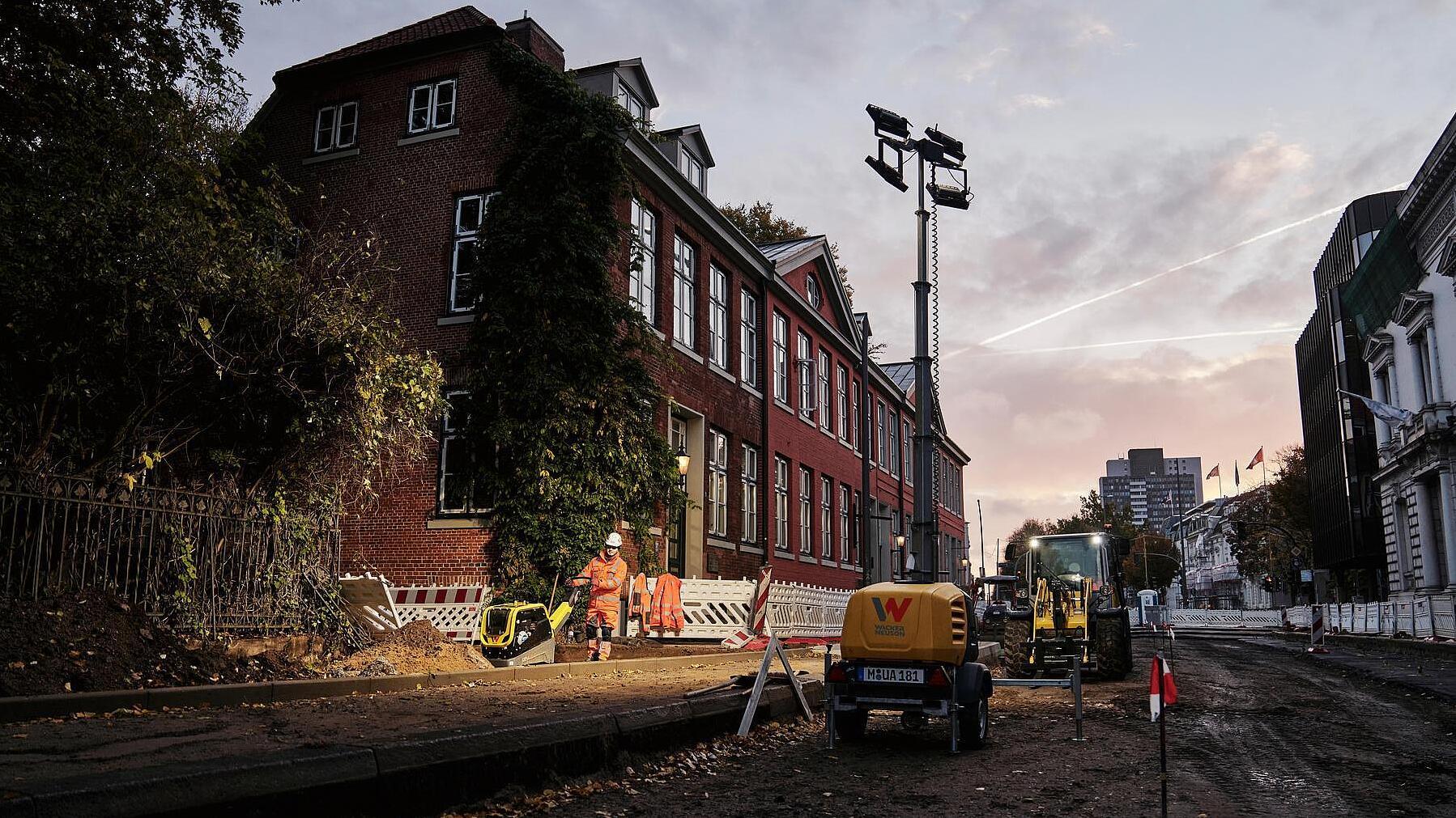 Obras al amanecer, trabajador trabajando bajo una torre de iluminación.