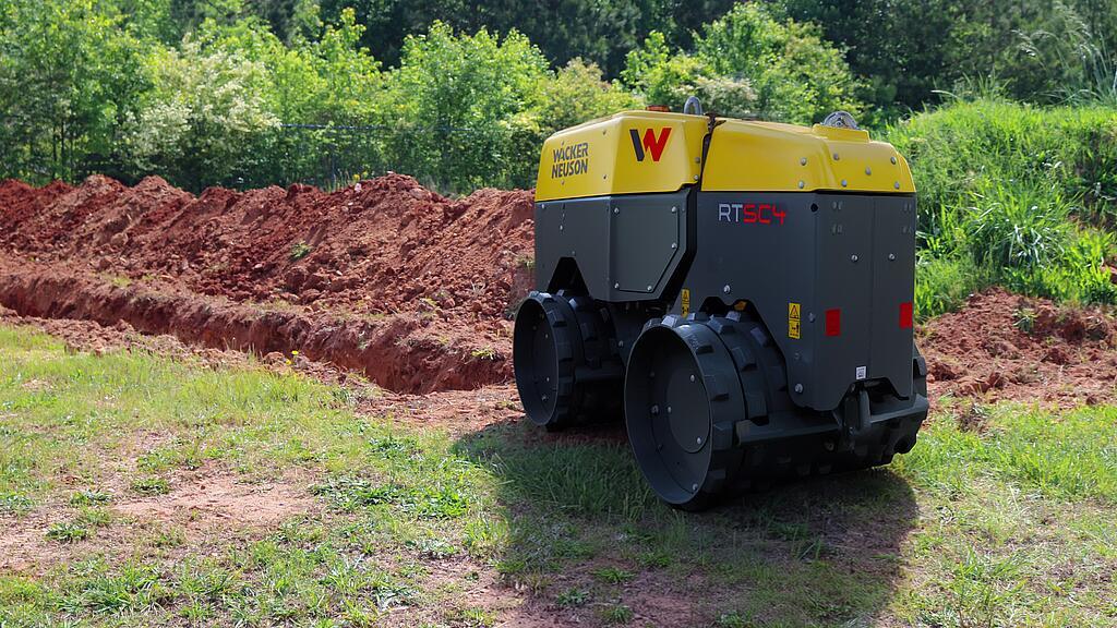 Grabenwalze von Wacker Neuson auf Baustelle neben frisch gezogenem Graben im Grünen