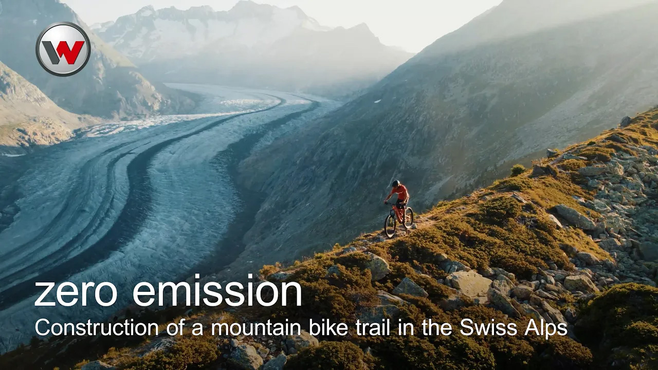 Un hombre montando en bicicleta de montaña por la cresta de una montaña, con montañas nevadas al fondo